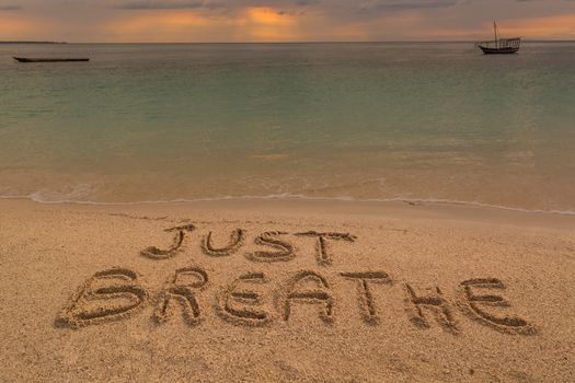 In the picture a beach at sunset with the words on the sand "Just breathe".