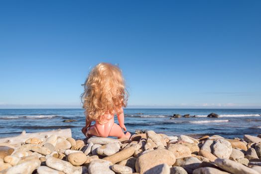 Plastic Baby Doll with blonde long hair sitting on the seashore