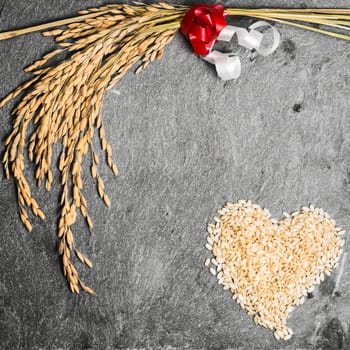 In the picture an ear of wheat and a heart formed by grains of rice on background of  stone.