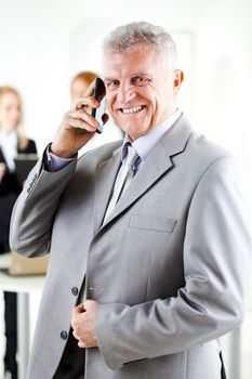 Happy senior businessman talking on mobile phone in the office. Looking at camera. Selective Focus.