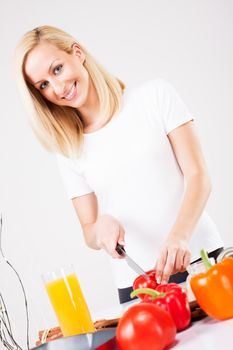 Happy young beautiful woman cutting tomato in the kitchen.