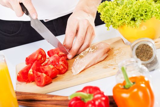 Cutting tomato and chicken breast in the cutting board.
