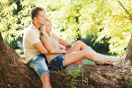 Beautiful embraced romantic couple in the park sitting on the tree.