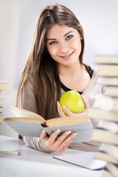 Beautiful Student girl sitting with apple between many books and learning.