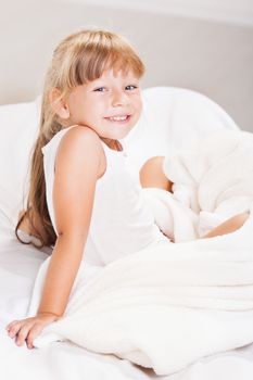 Cute little girl sitting on the bed in the morning.