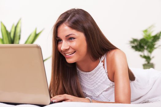 Teenage girl lying on bed and using laptop.