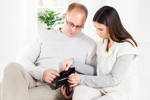 Young couple sitting worried in living room with Empty wallet. 