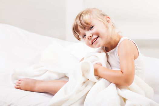 Cute little girl sitting on the bed in the morning.