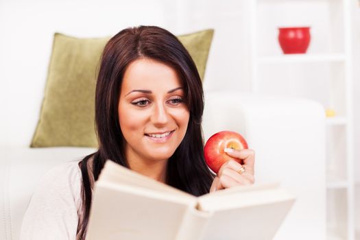 Beautiful young woman resting with book and apple at home.