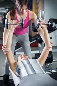 Cute Sporty young woman doing exercise in a fitness center with her personal coach. She is working exercises to strengthen her chest.