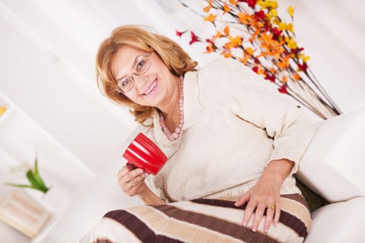 Senior woman sitting in living room and drinking coffee.
