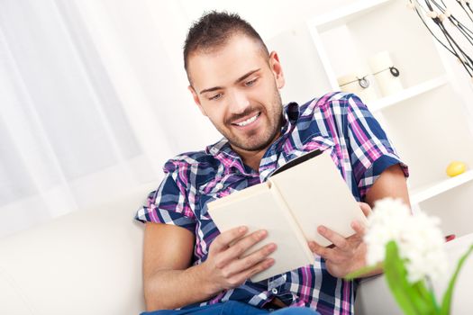 Beautiful young man resting with book at home.