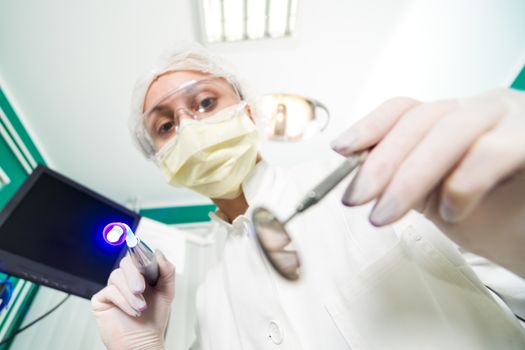 Dentist holding dental laser system and Angled Mirror for inspecting a patient. Selective Focus.