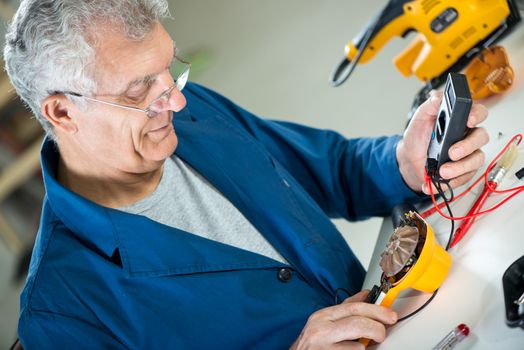 Senior adult Electrician using Digital Voltmeter for Testing Voltage on old hair dryer.