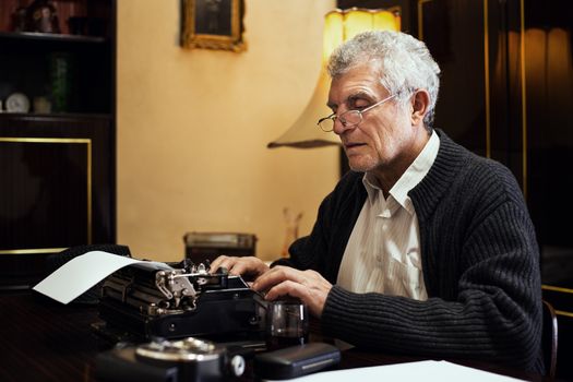 Retro Senior man writer with glasses writing on Obsolete Typewriter.