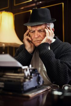 Worried Retro Senior Man writer with hat sitting at the Desk and thinking.