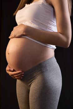 Pregnant woman on black background holding her belly.