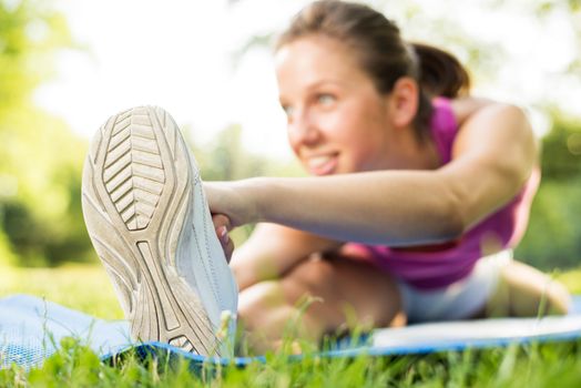 Cute young woman doing stretching exercises in the park. Selective Focus, focus on the shoe.