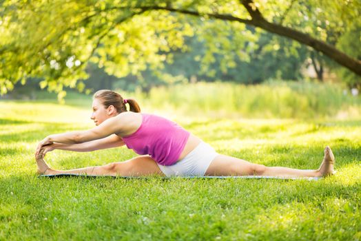 Beautiful young woman doing relaxing and stretching exercises in the park.