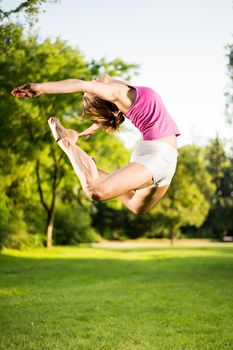 Beautiful young woman jumping in the park. She is doing Sheep Jump.