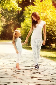 Beautiful mother and daughter walking through a park on spring day.