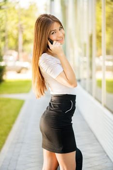 Happy Businesswoman standing on the street, holding business bag and using a Cell Phone.