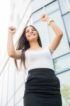 Successful Businesswoman standing on the street in front of Office Building with Arms Raised.