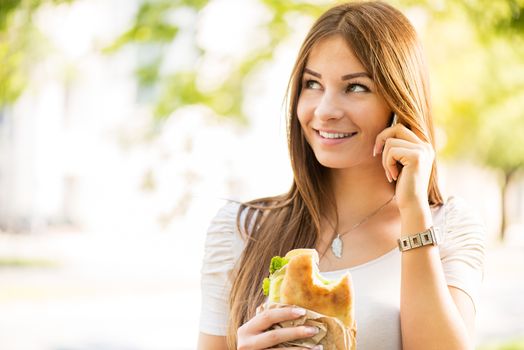 Portrait of beautiful, smiling young woman taking a break for breakfast and using a Cell Phone.