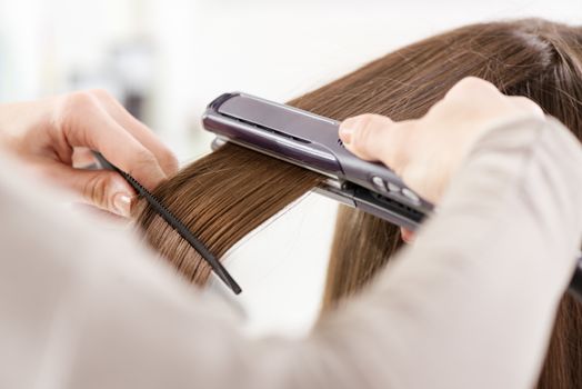 Hairdresser straightening long brown hair with hair irons.