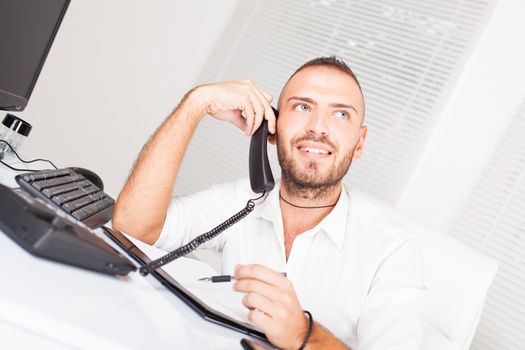 Attractive businessman sitting at the table and talking on the telephone.