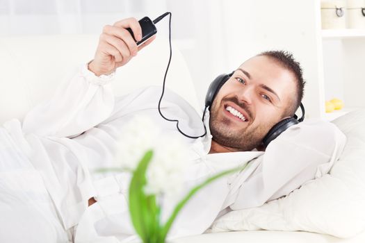 Beautiful young man resting and listening music at home.