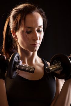 Portrait of a beautiful woman exercising with dumbbells on black background.