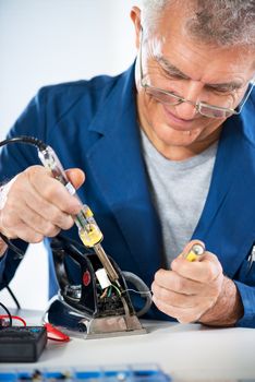 Senior adult Electrician repairing old iron with soldering iron.