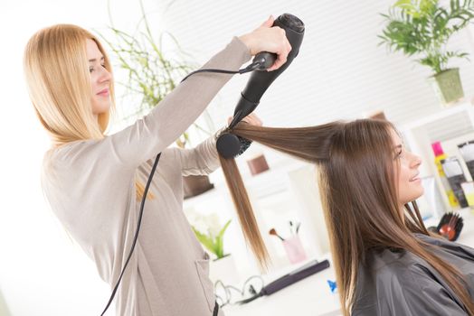 Hairdresser drying long brown hair with hair dryer and round brush.