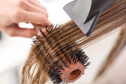 Drying long brown hair with hair dryer and round brush. Close-up.