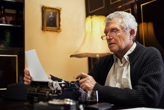 Retro Senior man writer with glasses writing on Obsolete Typewriter.