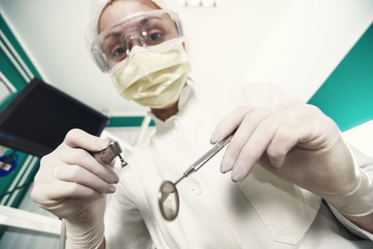 Dentist holding dental drill and Angled Mirror for inspecting a patient. Selective Focus.