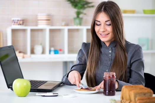 Businesswoman in the kitchen preparing breakfast. She is smearing jam on bread before going to work.