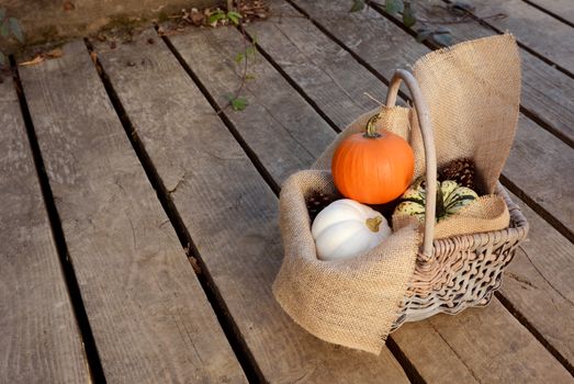 Small pumpkins in a hessian-lined basket outside on a wooden walkway