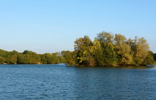 Barden Lake at Haysden Country Park, Tonbridge. Trees on a small island catch the afternoon sun.