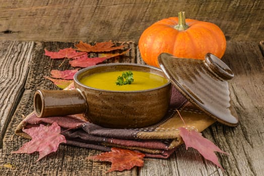Bowl of creamy homemade pumpkin soup on an autumn themed background.