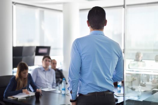 Business man making a presentation at office. Business executive delivering a presentation to his colleagues during meeting or in-house business training. Rear view. Shalow depth of field.