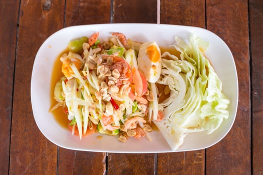 Green papaya salad with salted egg on wood table. Original spicy thai food is the most popular