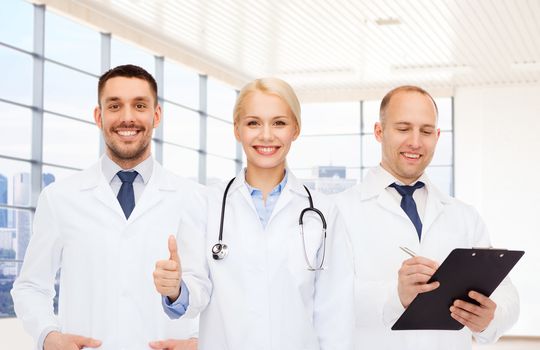 healthcare, people, gesture and medicine concept - group of doctors with stethoscope and clipboard showing thumbs up over clinic background