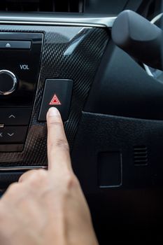 Closeup of young woman pressing emergency button on car sport dashboard.