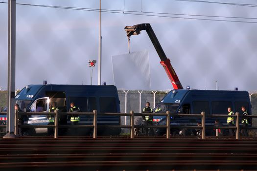 FRANCE, Calais: Police officers watch as workers install new fences around the French entrance of the Channel Tunnel in Calais, northern France, on October 26, 2015. Since the beginning of the migrants crisis, railway company Eurotunnel has reinforced its security measures, including installing new fences to avoid migrants enter the site.