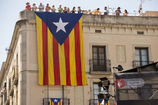 Barcelona, Spain - September 20, 2015: A large Catalan flag , a symbol of Calalonian independence, hangs below onlookers watching the the La Merce performances in Sant Jaume Square.
