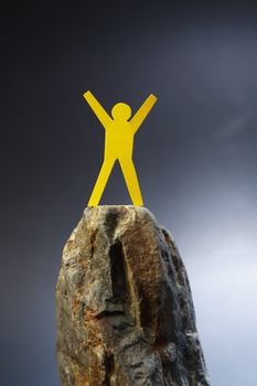 Yellow paper man standing on the rock against dark background