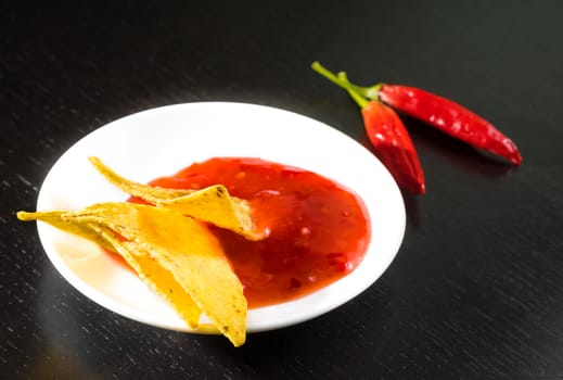 crisp corn nachos with spicy hot tomato sauce as a snack or appetizer in a white disc on black wood table