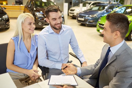 auto business, sale and people concept - happy couple with dealer buying car in auto show or salon